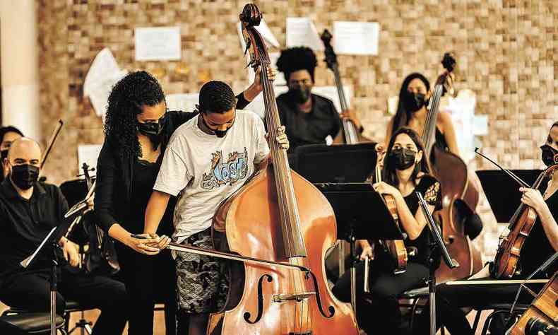 Jovens alunos tocam instrumentos de concerto, monitorados por msicos, em projeto da Orquestra Ouro Preto