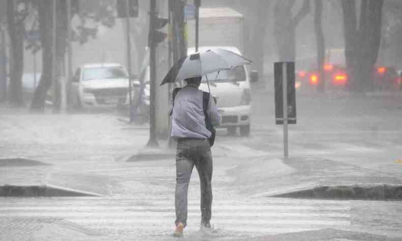 Homem caminha e atravessa rua na chuva