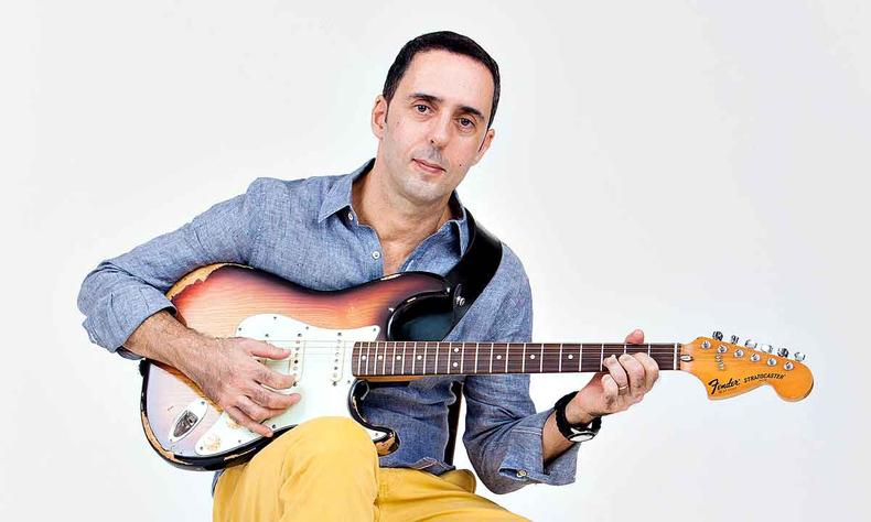 Affonsinho est sentado, toca guitarra e olha para a cmera 