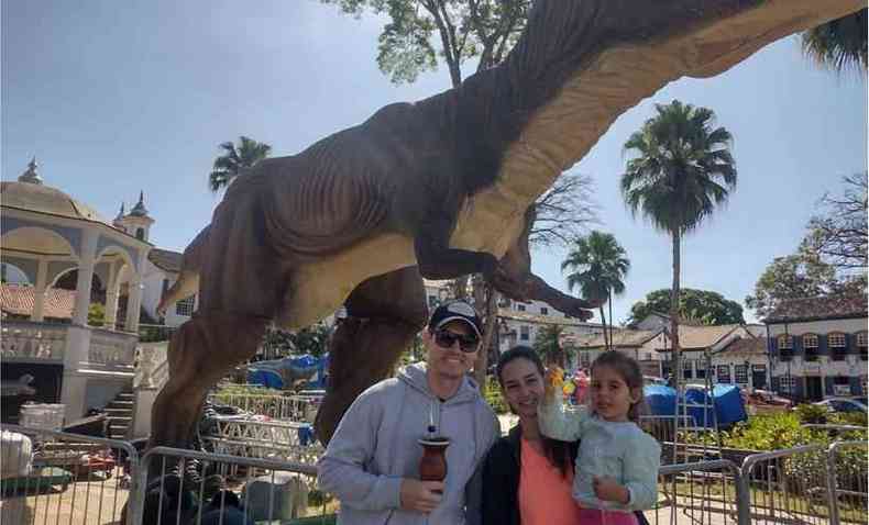 Pai, me e filha posam para foto diante de um dinossauro