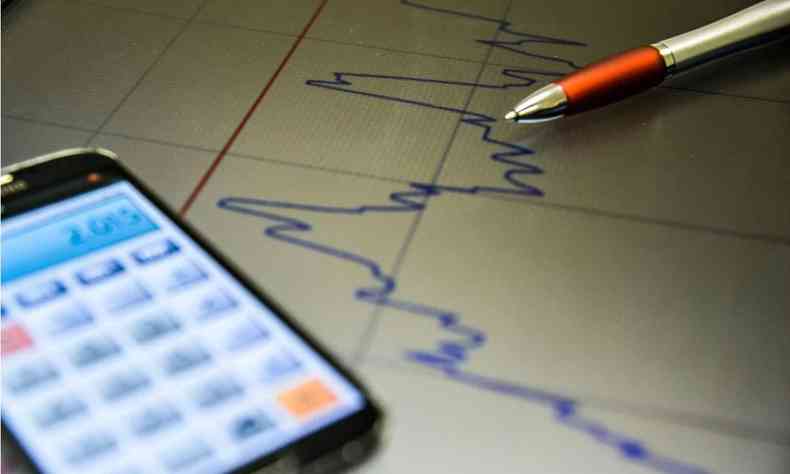 Celular com uma calculadora na tela e uma caneta azul desenhando um grfico crescente em um papel.