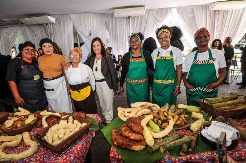 mulheres cozinheiras atrs de uma mesa cheia de guloseimas mineiras como biscoito papa-ovo e bolos