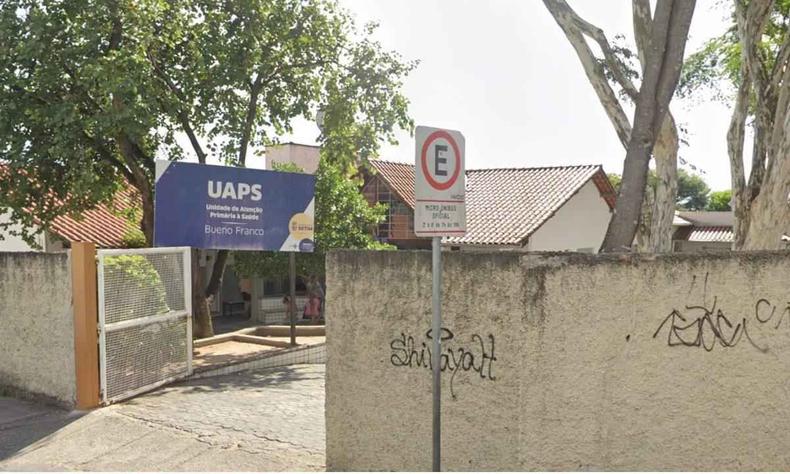 Fachada da unidade de sade Bueno Franco, com o porto aberto, rvores, um muro pichado e a placa azul da unidade