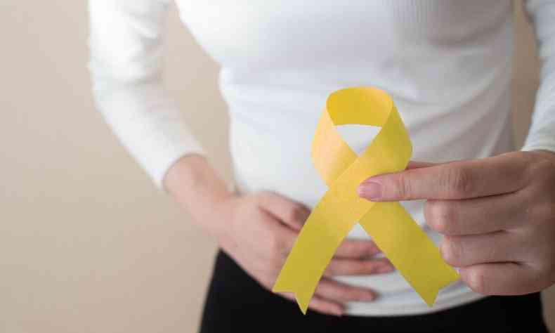 Foto da campanha de preveno da endometriose mostra, em primeiro plano, fita amarela e ao fundo mulher com a mo sobre a regio do tero 