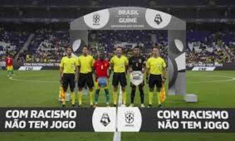 Jogadores e rbitros posam em frente a um cartaz onde se l 'Com racismo no tem jogo'