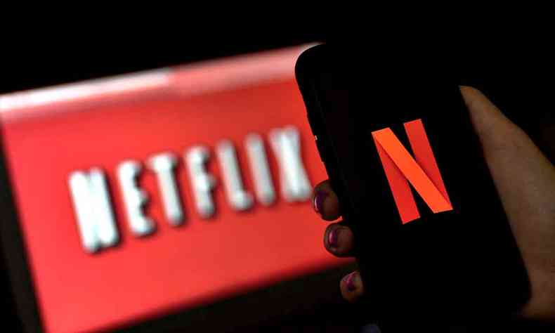 Homem segura celular, que mostra o logotipo da Netflix em letra vermelha