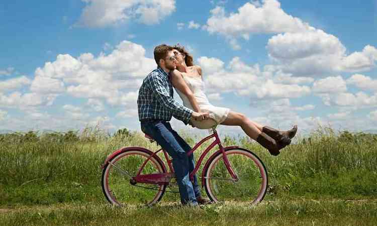 casal andando de bicicleta, com a mulher na frente dando um beijo no homem