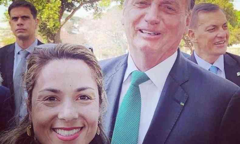 Uma selfie de Klio Hirano e do presidente Jair Bolsonaro. Ela  uma mulher branca e loira e sorri para a foto. No fundo, o presidente jair Bolsonaro aparece de terno sorrindo 