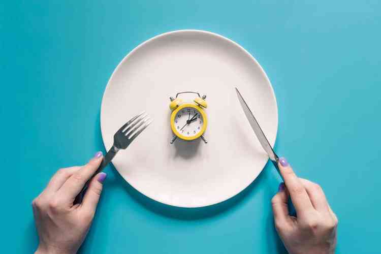 maos segurando faca e garfo acima do despertador em um prato sobre fundo azul