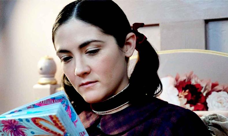 Sentada numa cama, a atriz Isabelle Fuhrman l um livro em cena de rf 2 - A origem 
