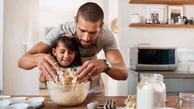 Pai e filha sorrindo enquanto cozinham juntos