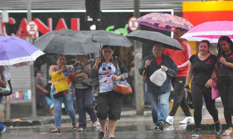 Pessoas segurando um guarda-chuva por causa do tempo chuvoso. Muitas cores podem ser vistas, vindo das roupas, guarda-chuva e das lojas ao fundo