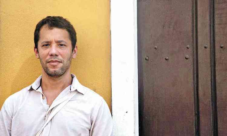 Escritor Itamar Vieira Junior olha para a cmera, encostado em parede amarela