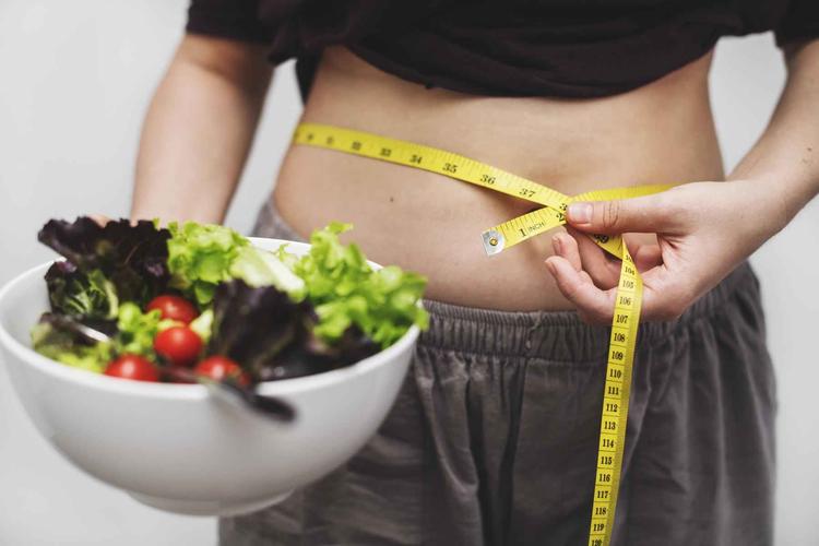 Mulher segurando uma salada e medindo a circunferncia da barriga