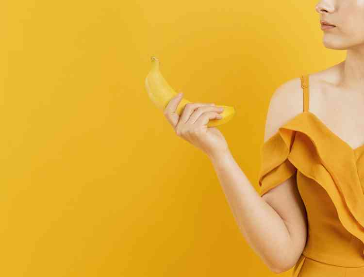 Mulher segurando uma banana em fundo amarelo