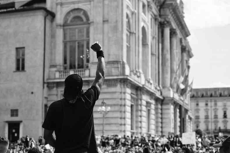 Imagem em preto e branco de um homem negro levantando sua mo com o punho fechado em frente a uma multido