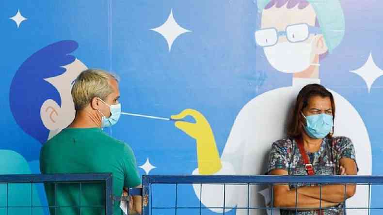 Homem e mulher com máscara na frente de um grafite de um profissional de saúde