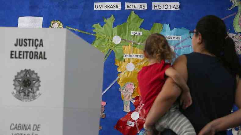Eleitora com a filha no colo, ao lado de uma sesso de votao, e em frente a um mapa do Brasil com o nome das 5 regies