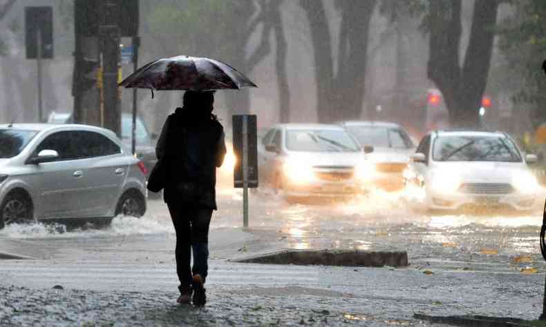 Forte chuva cai na tarde da capital mineira. Pessoa com um guarda-chuva e carros passando