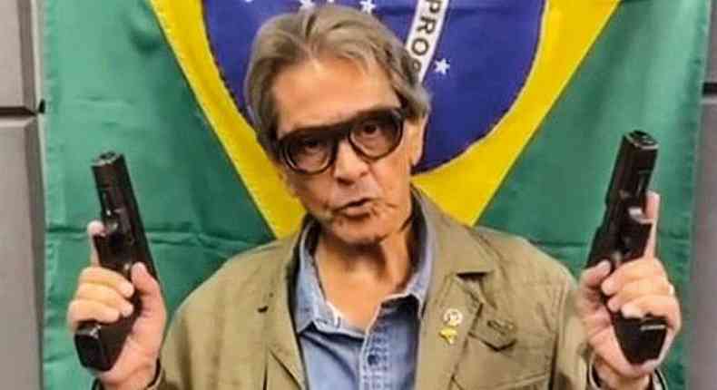 Roberto Jefferson segura duas armas na frente da bandeira do Brasil