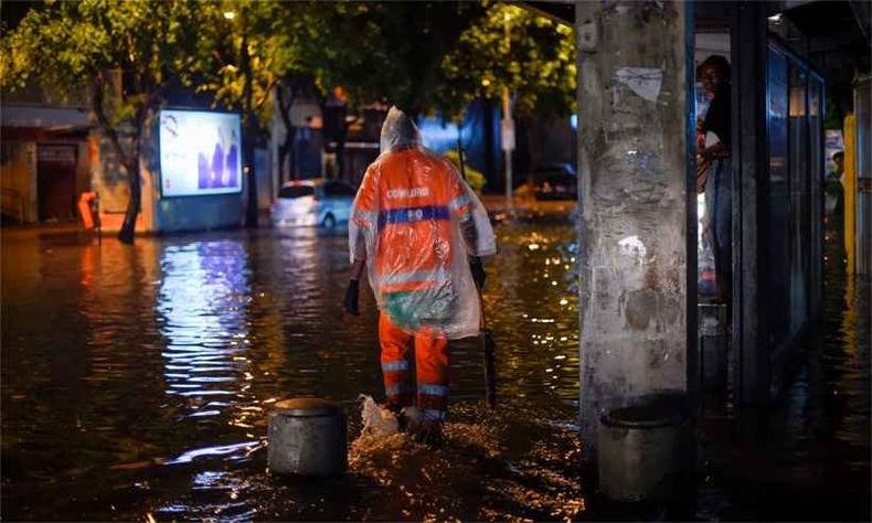 Agentes da Prefeitura do Rio percorremo Bairro de Botafogo, que teve vias inundadas, enquanto moradora se protege em cima de banco do ponto de �nibus (foto: AFP / Mauro Pimentel )