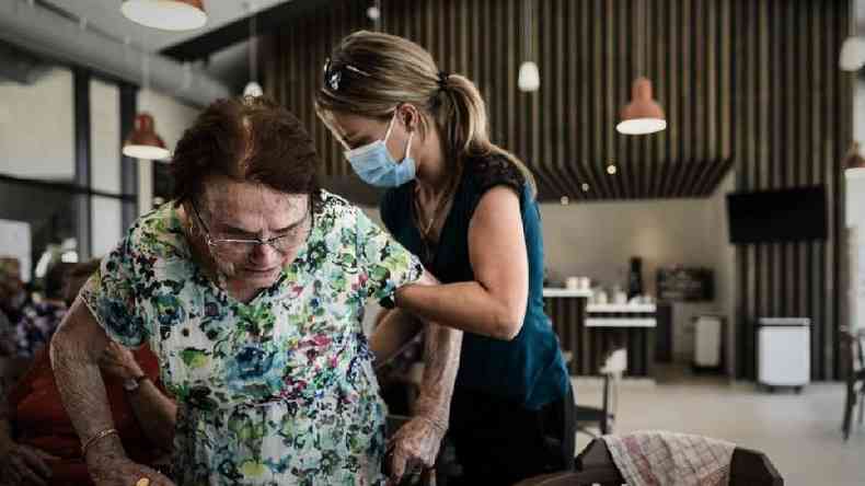 Um voluntrio ajuda a apoiar uma mulher em p acima de uma cadeira em uma mesa durante o almoo no site Landais Alzheimer para pacientes com Alzheimer em Dax, Frana