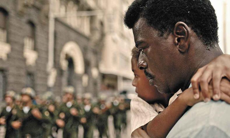 Seu Jorge carrega criana no colo, com policiais ao fundo, em cena do longa Mariguella