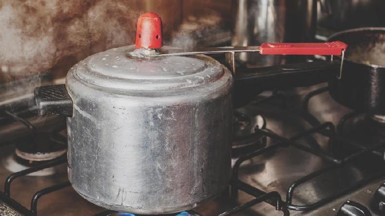 Panela de pressão de alumínio, no fogão, com fogo ligado e soltando vapor