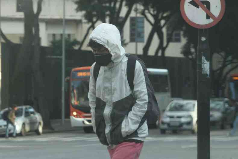 Homem caminha no centro de Belo Horizonte, com casaco cinza, capuz, e máscara. Esconde as mãos nos bolsos para suportar o frio