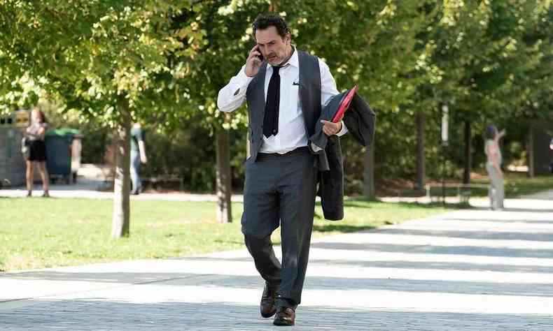 Com camisa branca, cala e gravata pretas, segurando pasta em uma das mos, gilles lellouche fala ao celular em cena do filme golias