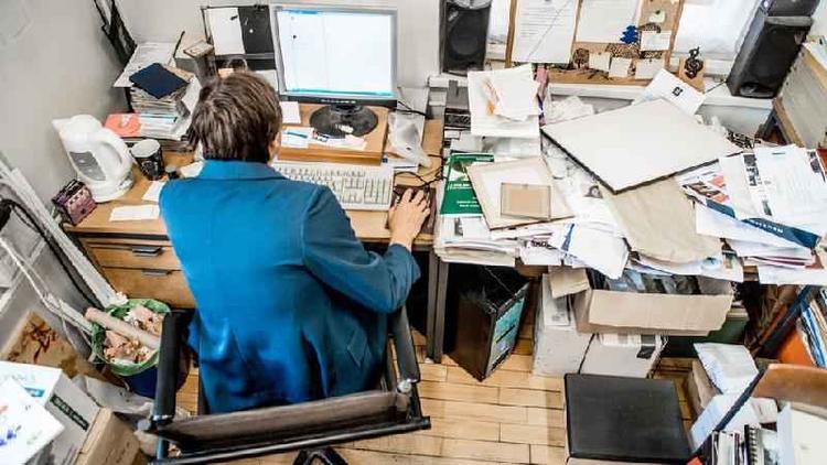 Pessoa sentada em mesa de escritório completamente bagunçada