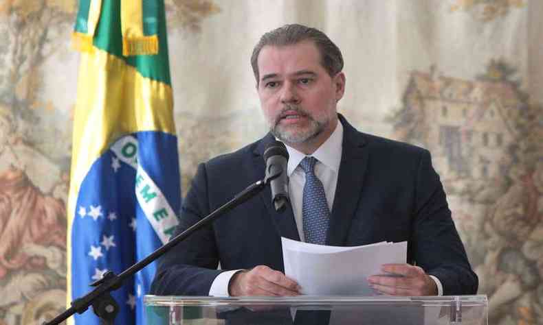 Dias Toffoli fala ao microfone; ao seu lado, uma bandeira do Brasil