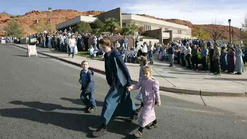 Dezenas de mrmons em frente a tribunal; uma mulher com filhos atravessa a rua no primeiro plano da foto