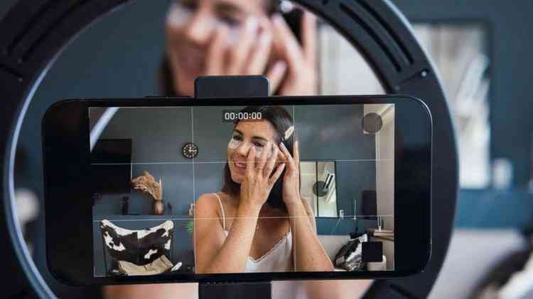 Mulher passando maquiagem no rosto em frente a celular