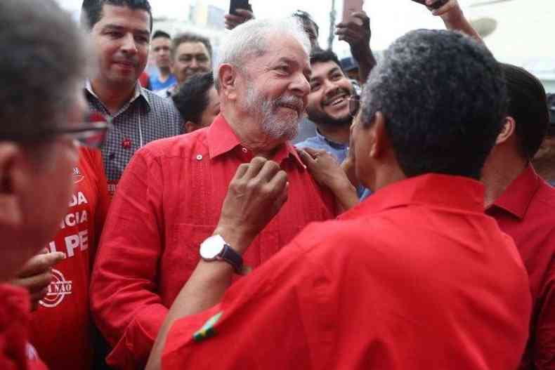Com camisa vermelha, Lula sorri no meio de apoiadores