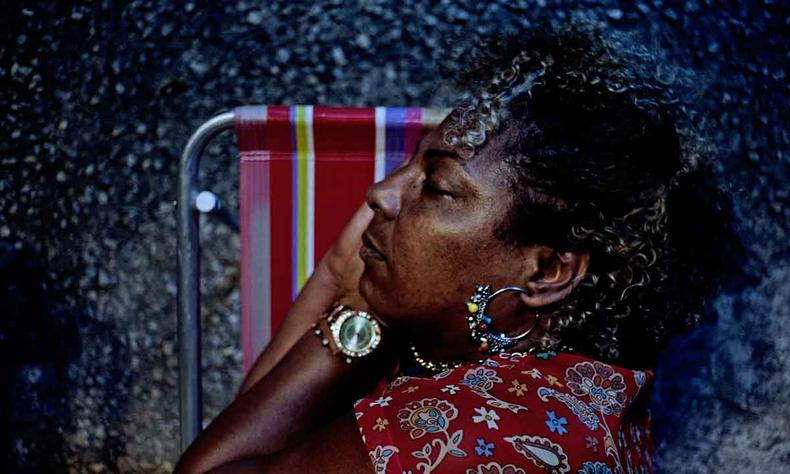 Usando brinco de argola com contas coloridas, atriz Rejane Faria dorme, com os braos atrs da cabea, em cadeira de praia, no filme Marte Um 