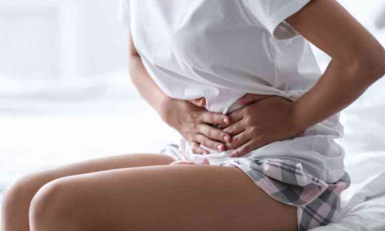 Mulher sentada na cama com a mo sobre a barriga, em crise de endometriose 