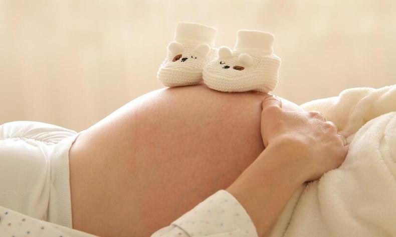 (foto: Marjon Besteman/Pixabay ) mão grávida, deitada, com um par de sapatinhos em cima da barriga