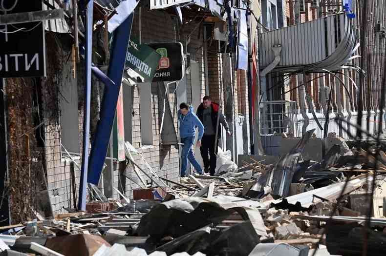 Homens caminham entre escombros de prdio em Kiev