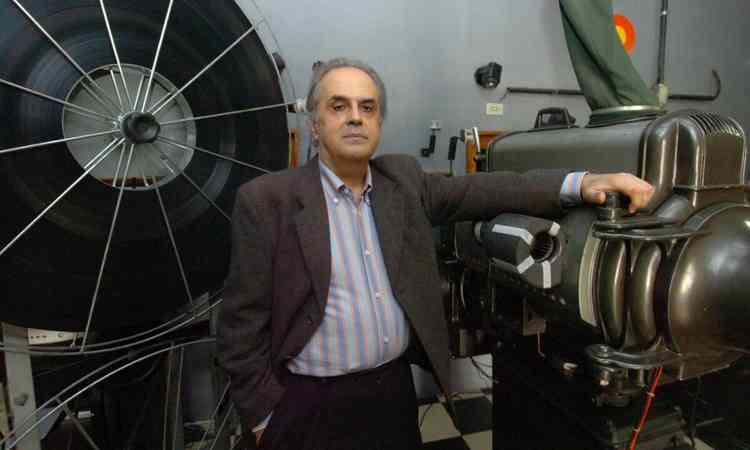 Geraldo Veloso olha para a cmera e tem atrs de si imenso projetor de filmes