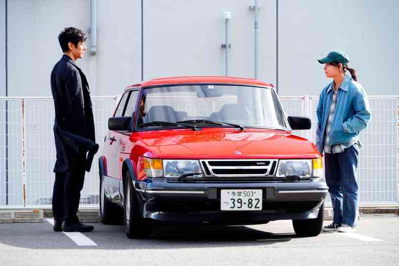 Cena do filme ''Drive my car'' tem automvel vermelho com ator  esquerda e mulher na porta direita