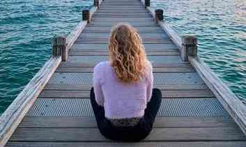 mulher, de costa,  sentada em um plataforma de frente para o mar