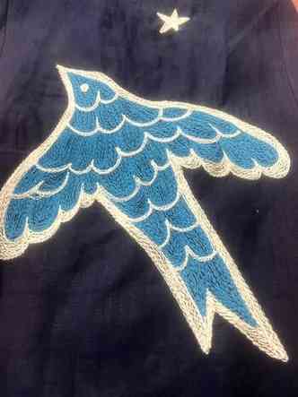 Pássaro azul claro bordado sobre pano azul-escuro, que remete à noite, no figurino criado por Ronaldo Fraga para Milton Nascimento
