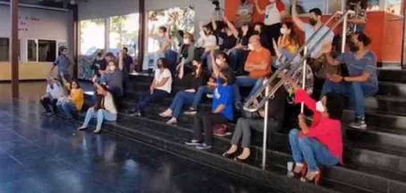 Técnicos administrativos, sentados em uma escada do CEFET-MG, levantam as mãos em votação para aprovar a deflagração da greve da categoria.