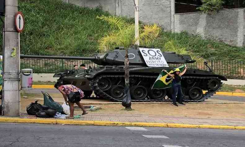 Bolsonarista em frente ao tanque de guerra com bandeira do Brasil sorrindo