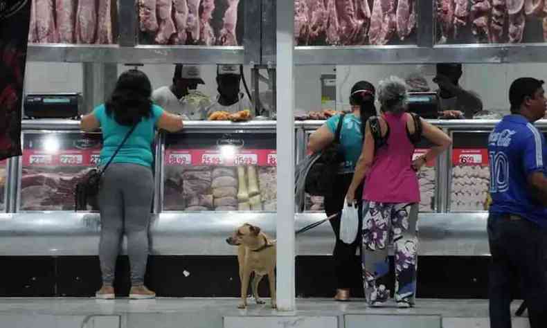 Na foto, é possível ver três pessoas comprando em um açougue de BH, os funcionários do estabelecimento e as carnes expostas no frigorífico. 