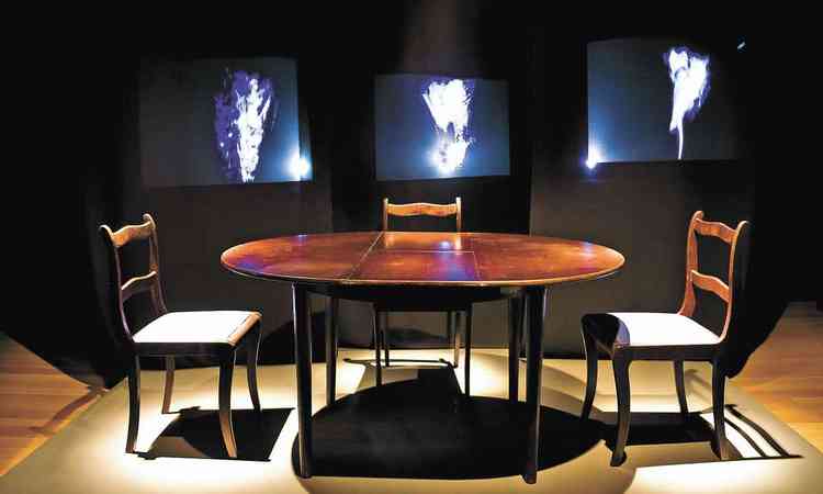 A instalao 'Cime', que tem monitores com imagens borradas atrs de mesa com cadeiras vazias
