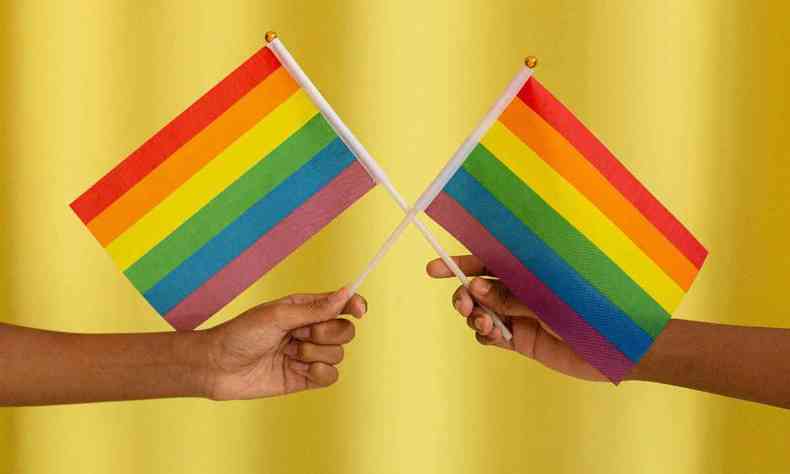 Mos segurando duas bandeiras LGBT cruzadas contra fundo amarelo