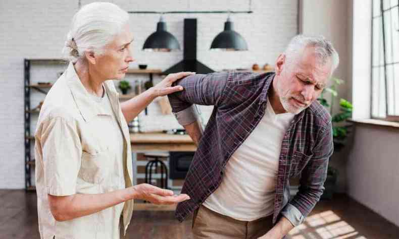 Homem idoso sentindo dor nas costas e sendo ajudado por sua esposa 