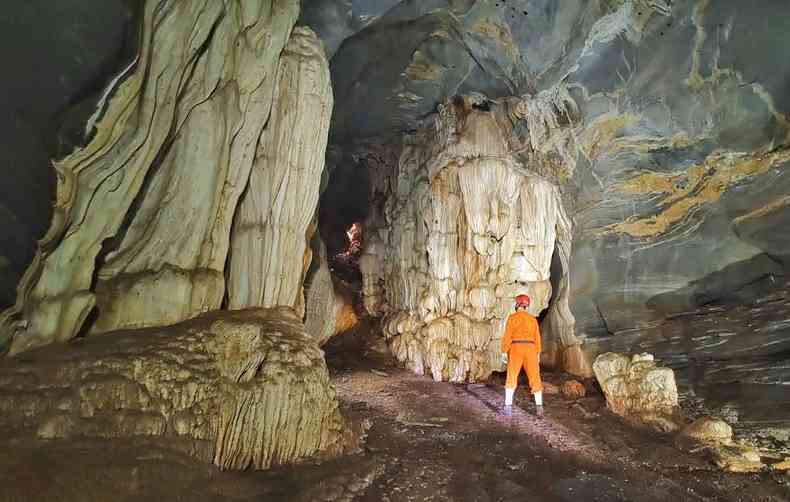 Pessoa de capacete e roupa alaranjada dentro de caverna